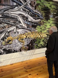 Gallery visitor with large printed collage and manatee skeleton sculpture
