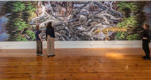 Gallery visitors and Christy with large printed collage and manatee skeleton sculpture
